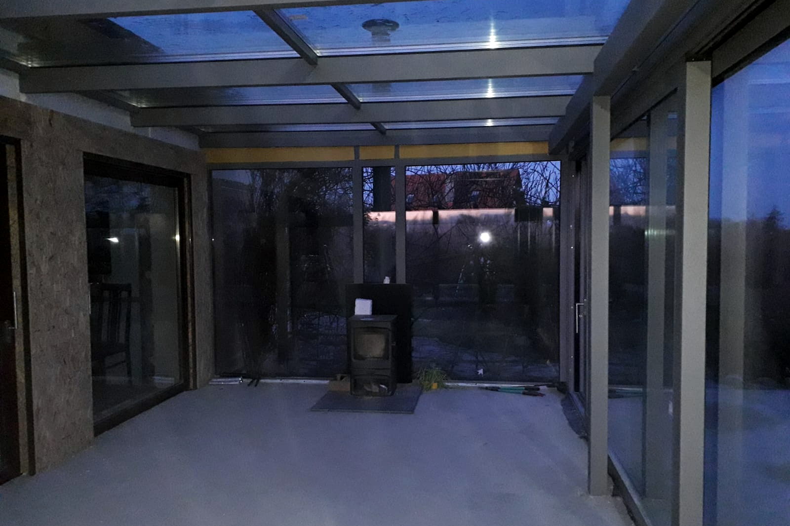 Interieur van de glazen tuinkamer met glasdak, schuifpui en uitzicht op de tuin.