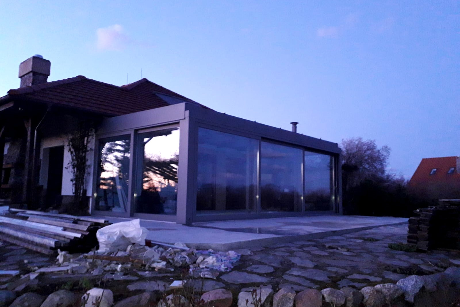 Glazen tuinkamer bij schemer, met verlichte glasvelden en de vijvertuin op de voorgrond.