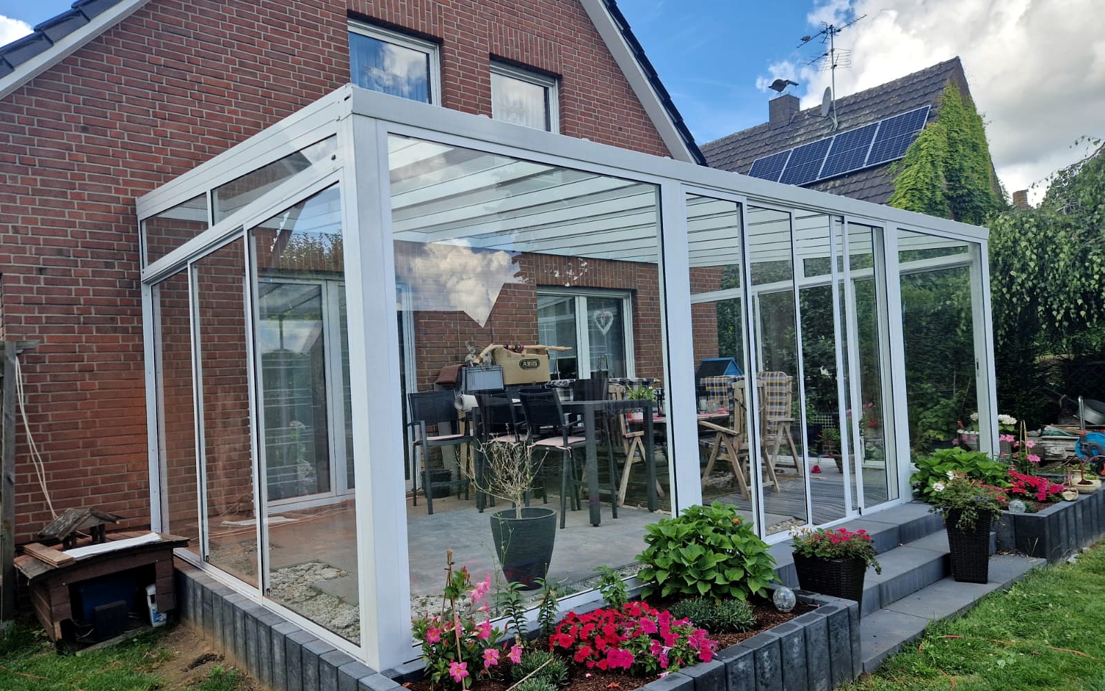 Witte wintertuin met glazen dak langs het terras van een bakstenen woning