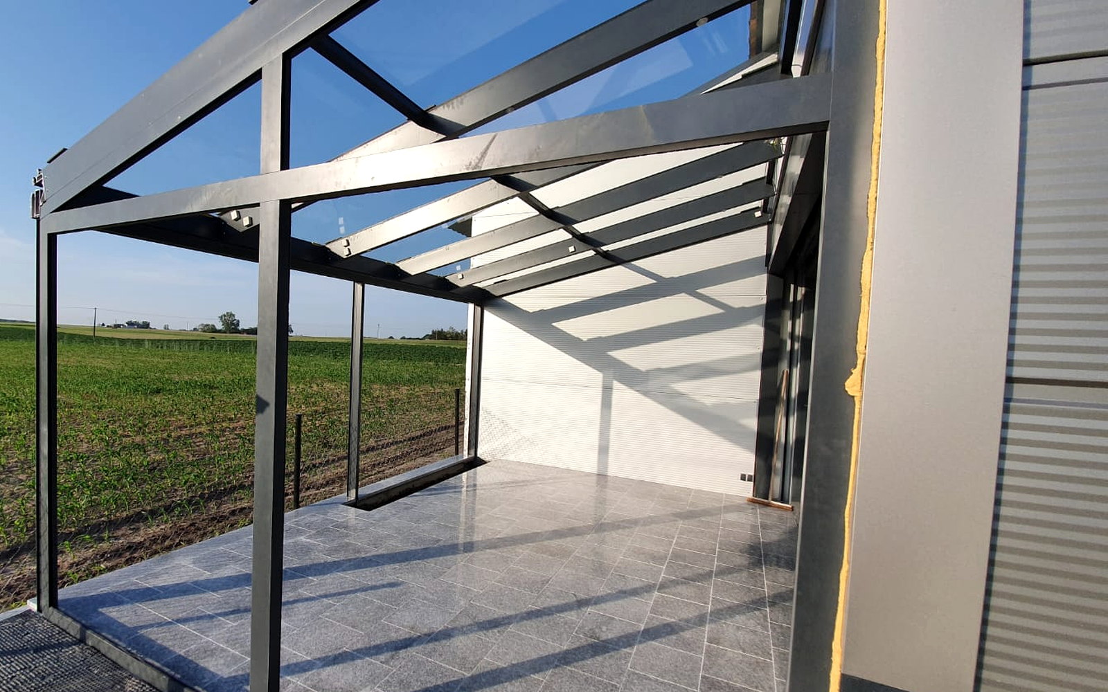 Glazen tuinkamer met aluminium liggers en glasdak, gezien vanaf het terras