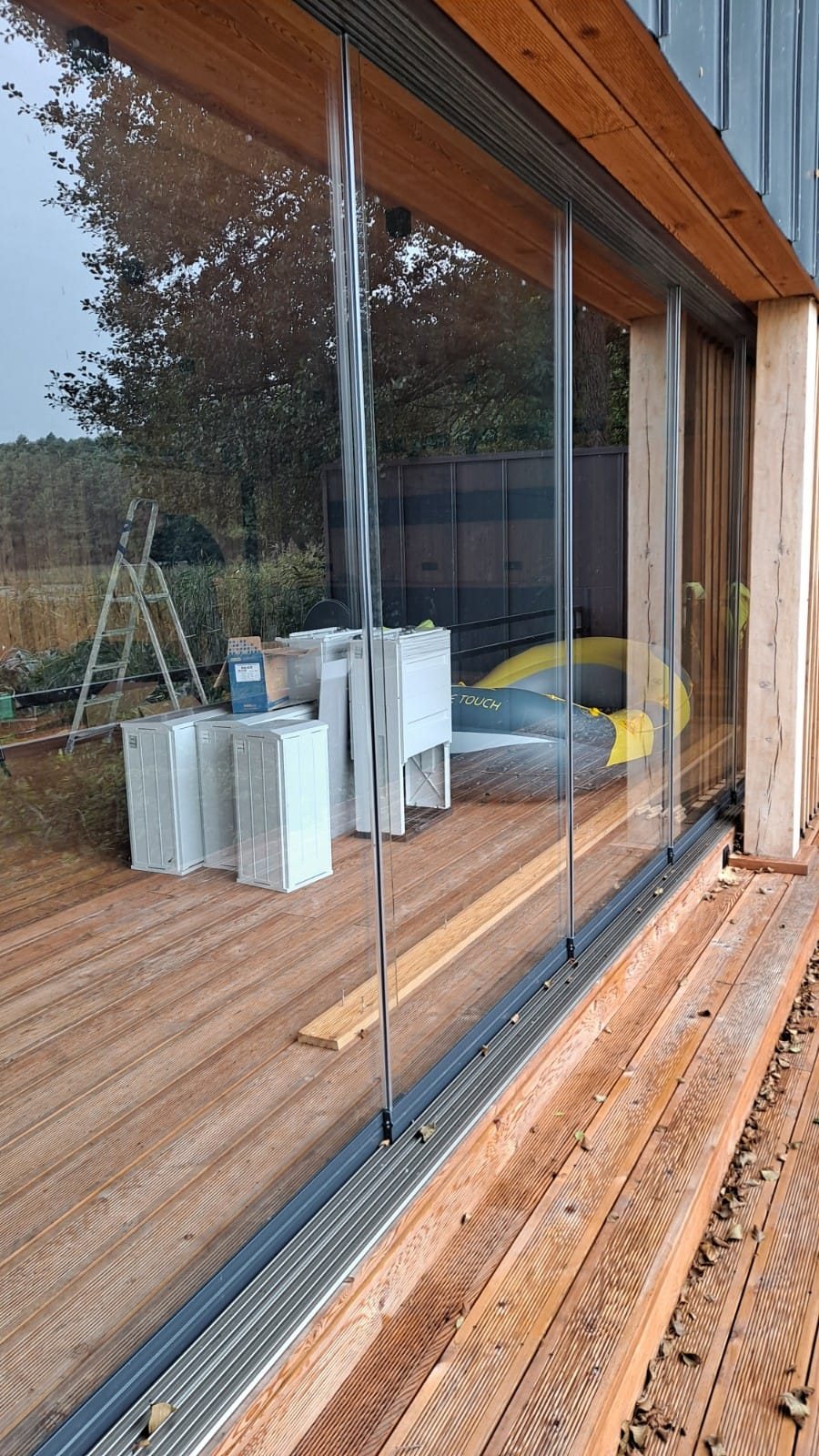 Randloze glazen schuifwand langs een houten terras.