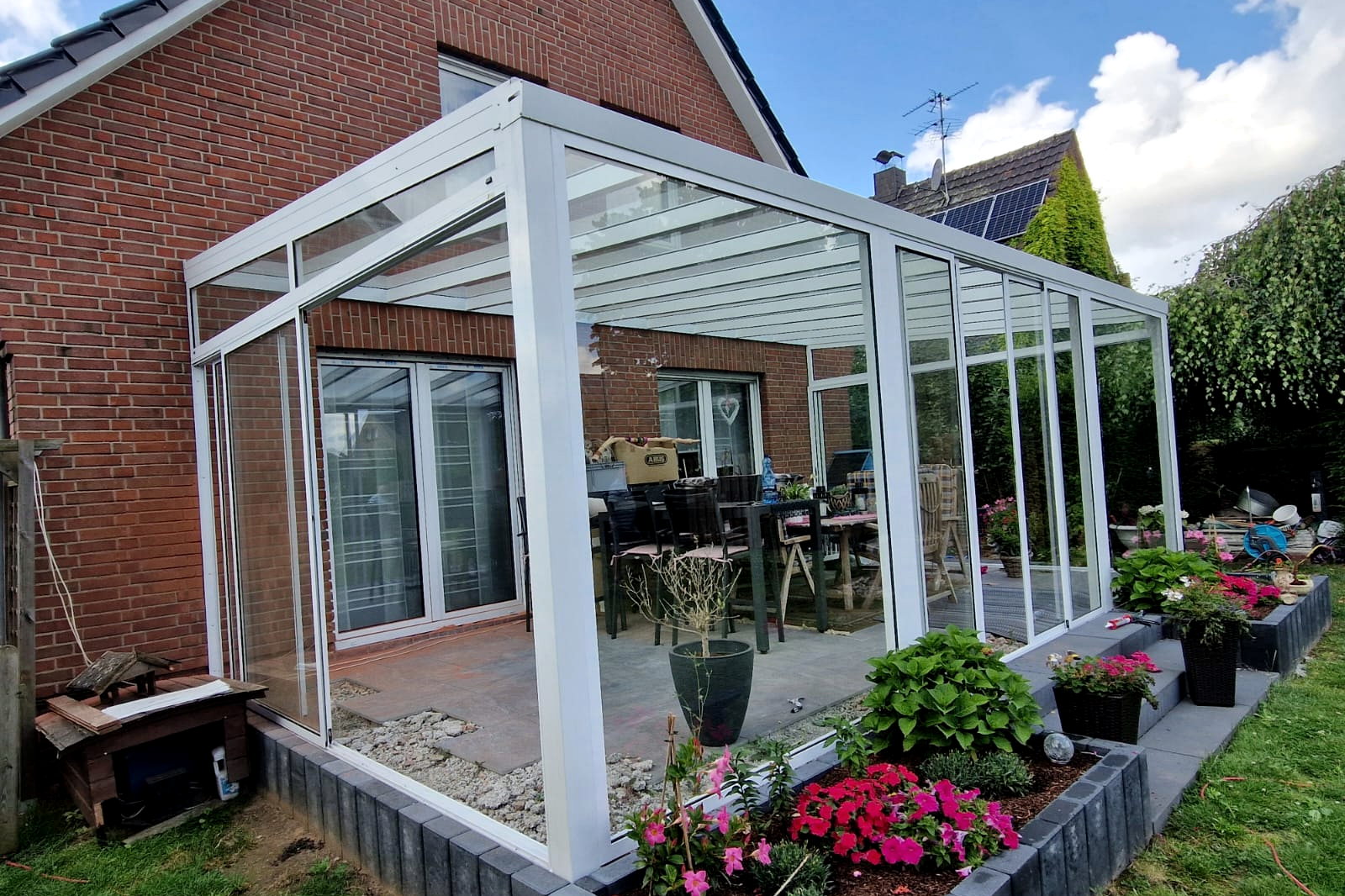 Vooraanzicht van de witte wintertuin met glazen schuifdeuren naar de tuin.