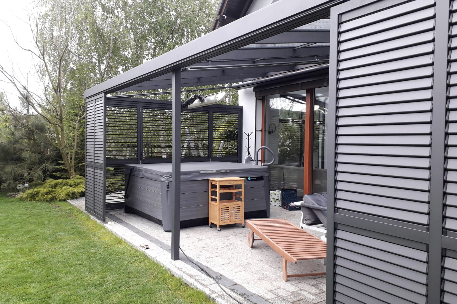 Terrasoverkapping met glasdak en verticale lamellenwand langs een tuin.