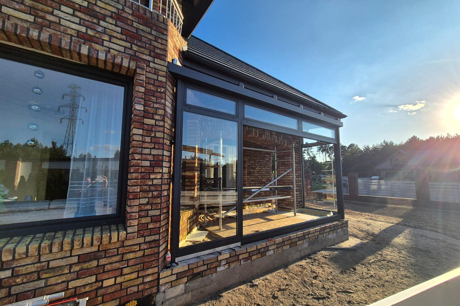 Zijaanzicht van de glazen aanbouw in laag avondlicht met de zon achter de gevel.