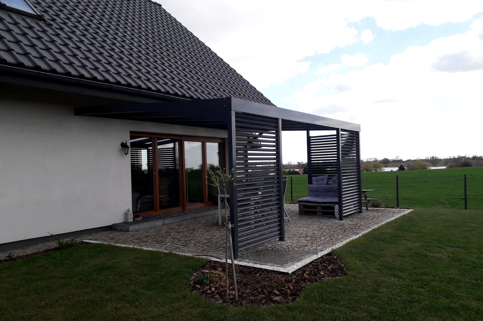 Overkapping met lamellen gezien vanuit de tuin, met de woning op de achtergrond.