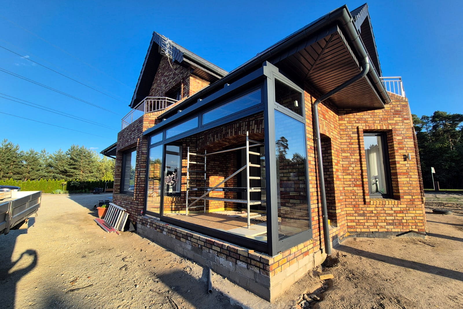 Glazen aanbouw met antracietgrijze aluminium profielen tegen een bakstenen nieuwbouwwoning onder een diepblauwe lucht.